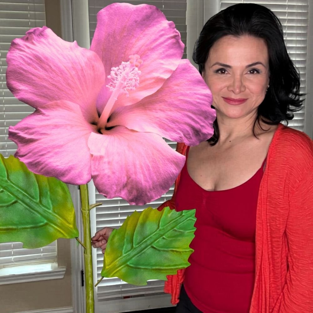 Woman holding giant pink and yellow hibiscus foam flower from luau party decorations DIY kit
