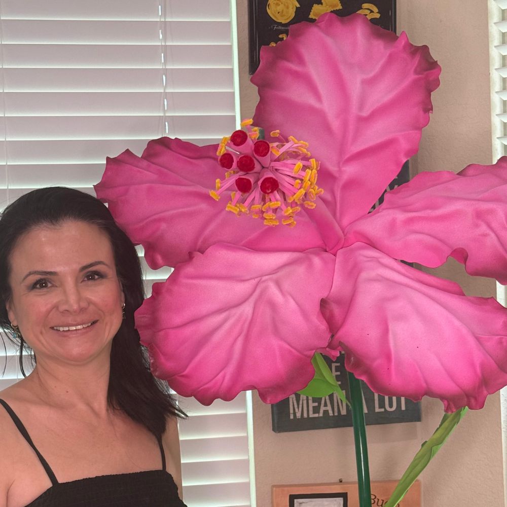 Woman holding giant pink and yellow hibiscus foam flower from luau party decorations DIY kit